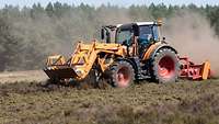 A member of the terrain management team drives a tractor with a mulcher on a field at a major training area.