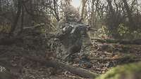Ein Soldat kniet an einem kleinen Bachlauf im Wald. Mit seinem G36 sichert er seinen Beobachtungsbereich.