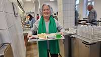 Eine Frau mit einem Mittagstablet in der Kantine auf dem ihr Essen und ein Getränk steht. 