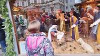 Ein Mädchen steht vor einer Holzkrippe auf dem Weihnachtsmarkt. 