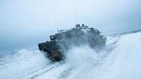 Ein deutscher Kampfpanzer der Typ-Klasse Leopard 2 fährt durch Schnee und Eis, dabei wirbelt er Schnee auf