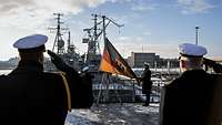 Zwei Marinesoldaten in Uniformmänteln halten eine schwarz-rot-goldene Flagge. Zwei weitere Soldaten grüßen diese militärisch.