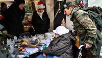 Eine Soldatin hilft einer Frau im Rollstuhl bei der Auswahl am Stand auf einem Weihnachtsmarkt.