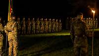 Etwa 65 Soldatinnen und Soldaten stehen nachts in Formation auf einer Wiese.