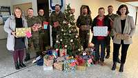 Gruppenfoto am Weihnachtsbaum mit Soldaten und Vertreterinnen und Vertretern der Caritas. Alle halten Geschenke in der Hand.