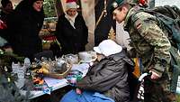 Eine Soldatin hilft einer Frau im Rollstuhl bei der Auswahl am Stand auf einem Weihnachtsmarkt.