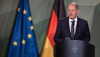 Olaf Scholz steht an einem Rednerpult, dahinter die Flagge Deutschlands und der EU.