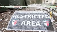 Ein verschneites Schild mit der Aufschrift „Restricted Area“ ist an einem Zaun angebracht