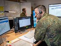 Soldiers working in a situation center look at monitors and make phone calls