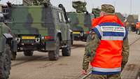 A soldier stands next to vehicles moving in a column