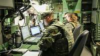 Several soldiers sit in a booth in front of computers