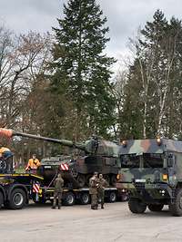 Two heavy-duty transporters loaded with tanks are parked on a street