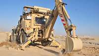 Ein großer sandfarbener Bagger steht auf Sand und schaufelt ein Loch