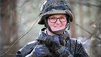 Soldier in field suit with combat helmet smiles at the camera.