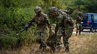 Two soldiers in fatigues hastily carry a wounded comrade out of the danger area.