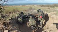 Three soldiers in a machine gun position in dunes, one is an instructor. In the background the sea.