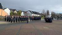 Auf einem Platz gedenken Soldaten in Formation mit einem Musikkorps einem Kameraden.