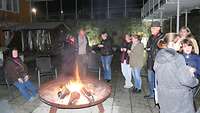 Eine Gruppe Menschen unterhält sich an einer Feuerstelle und trinkt Glühwein.