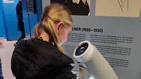 Ein Mädchen schaut in ein Mikroskop und hat Spaß dbei