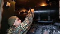 Ein Soldat setzt einen neuen sauberen Luftfilter in den Dieselgenerator ein. Dieser ist rund und zylindrisch geformt.