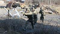 Vier Soldaten laufen mit den Gewehren im Anschlag zwischen Stacheldraht auf ein Haus zu