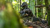 Ein Soldat im Wald mit Mundschutz und Gewehr im Anschlag