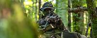 Ein Soldat im Wald mit Mundschutz und Gewehr im Anschlag
