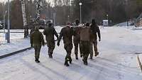 Auf einer verschneiten Straße transportiert eine Gruppe von Soldaten eine Trage mit einem Verwundeten
