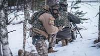 Zwei Soldaten knien im Schnee, der im Vordergrund kniende Soldat setzt einen Funkspruch an das Luftfahrzeug ab