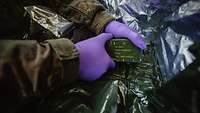 Ein Soldat hält mit speziellen Handschuhen eine Packung Sprengstoff.