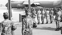 Schwarzweißbild: Soldaten verschiedener Nationen sind vor einem Flugzeug angetreten.