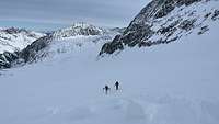 Zwei Ski-Bergsteiger stehen auf einem Schneefeld in Mitten der Bergketten.