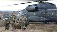Vier Soldaten tragen einen Verwundeten in einer Plane zu einem Hubschrauber, der bereitsteht.