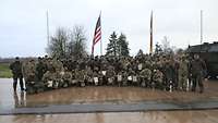 Deutsche und amerikanische Soldaten mit Urkunden stehen und knien vor den Flaggenmasten. 