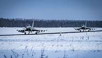 Zwei Eurofighter fahren auf einem Rollfeld. Es ist Winter und überall liegt Schnee.