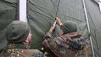 Zwei Soldaten zurren ein Zeltplanenband ein.