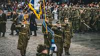 Soldaten in grün-brauner Paradeuniform mit Offiziersäbeln marschieren während der Parade.