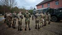 Mehrere Soldaten stehen im Halbkreis um einen Soldaten herum, seitlich von ihnen ein Lkw.