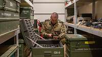 Der Soldat hockt sich hin, um ein Funkgerät zusammenzusetzen. Er ist in einem Container umgeben von Schwerlastregalen.