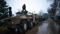 Radpanzer und Lastwagen stehen im Regen hintereinander auf einer Straße.