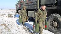 Zwei Soldaten tragen jeweils zwei Benzinkanister über ein Feld.