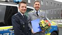 Ein Polizist und ein Soldat mit einem Blumenstrauß stehen vor einem Polizeiauto.