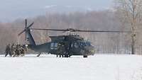 Eine Gruppe Soldatinnen und Soldaten trägt einen Verwundeten durch den Schnee zu einem gelandeten Hubschrauber.