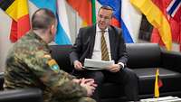 Boris Pistorius sitzt einem Soldaten im Gespräch gegenüber, hinter ihm Flaggen der NATO Mitgliedsstaaten.
