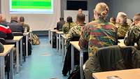 Soldiers of different nations sit at tables in 6 rows of seats.