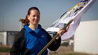 Eine deutsche Sportlerin läuft mit der Flagge in der Hand die Straße entlang. 