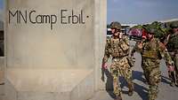 Das Team aus Soldaten läuft entlang einer hohen Betonmauer, auf der „MN Camp Erbil“ steht