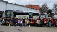 Eine Gruppe Menschen aufgestellt vor vier Bussen. 