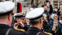 Eine Marinesoldatin in dunkelblauer Uniform und mit weißer Schirmmütze spielt eine Piccolo-Flöte.