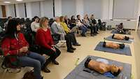 Mehrere Frauen sitzen in einem Saal und üben an Übungspuppen die Herzdruck-Massage. 